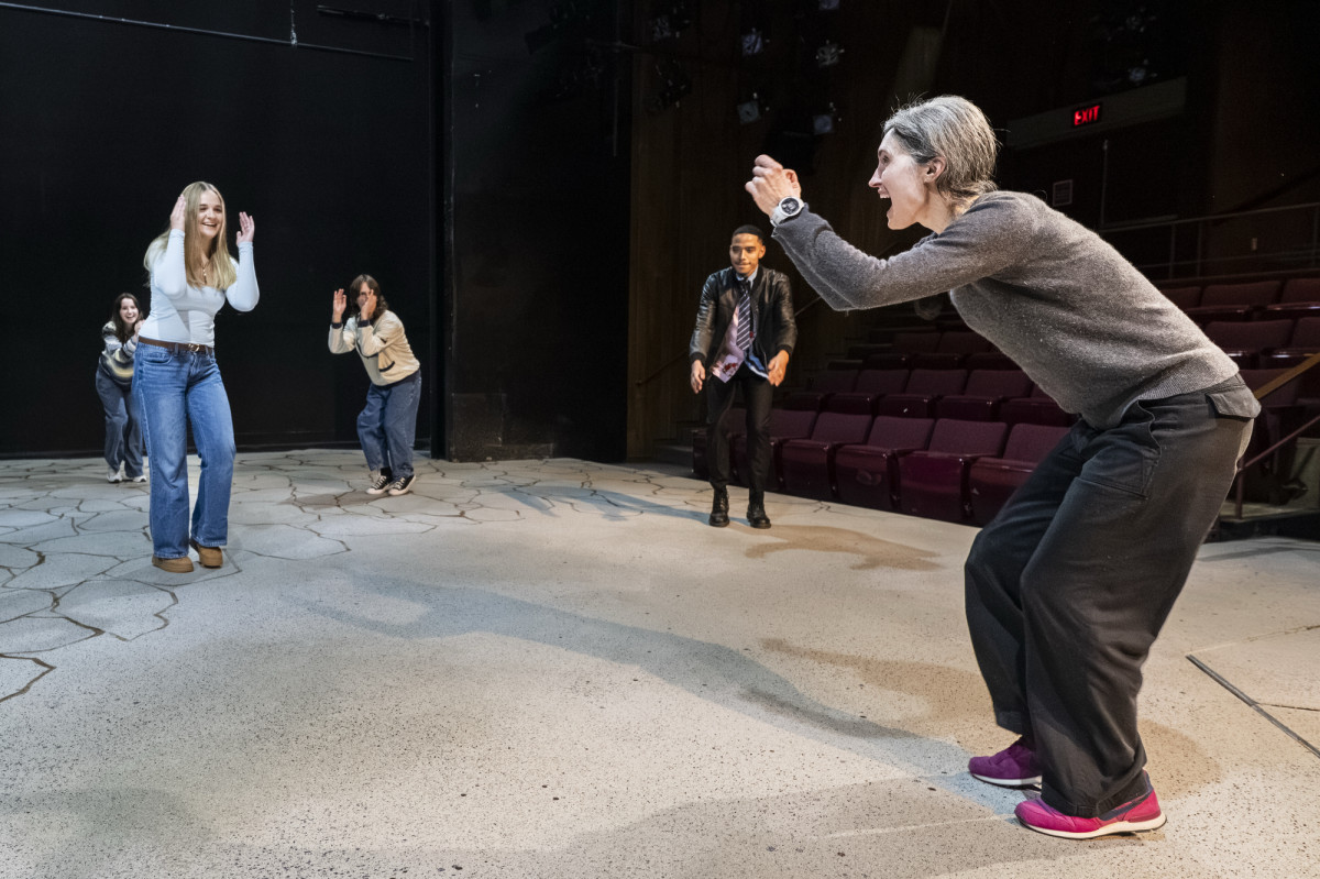 Colleen Conroy is in motion on stage and she teachers her students about movement and voice exercises. Her students, also on stage mimic her movement.