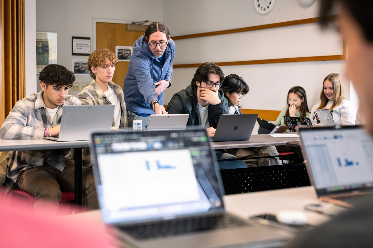 Green stands next to a student and points to a laptop to explain what is being shown on the screen.