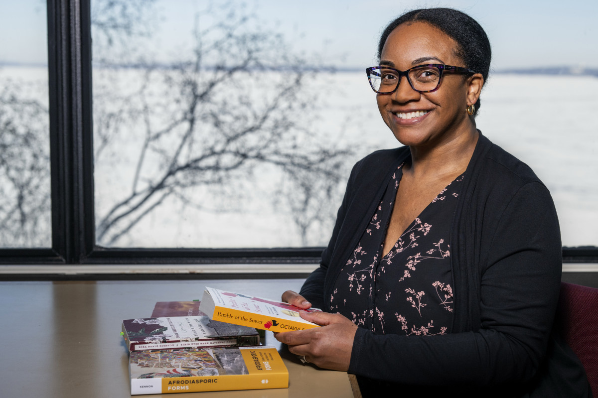 Raquel Kennon sits at a table in front of a large window. She holds a book in her hands while posing for the photo.