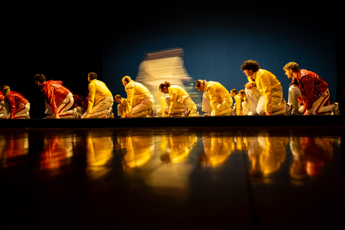 Students perform a choreographed dance as a group on a stage.