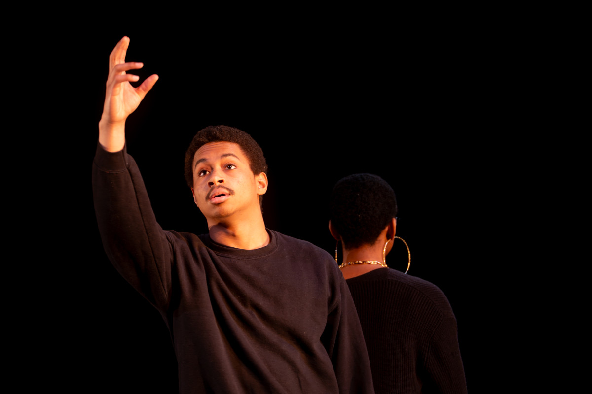 A student stands back to back with another dance student and reaches up to the ceiling during a dance performance.