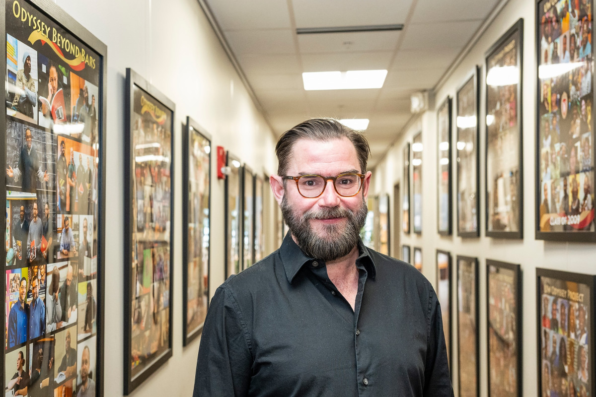 Kevin Mullen stands in a hallway. Along the walls are photographs of students who have graduated from the Odyssey program over the past several years.