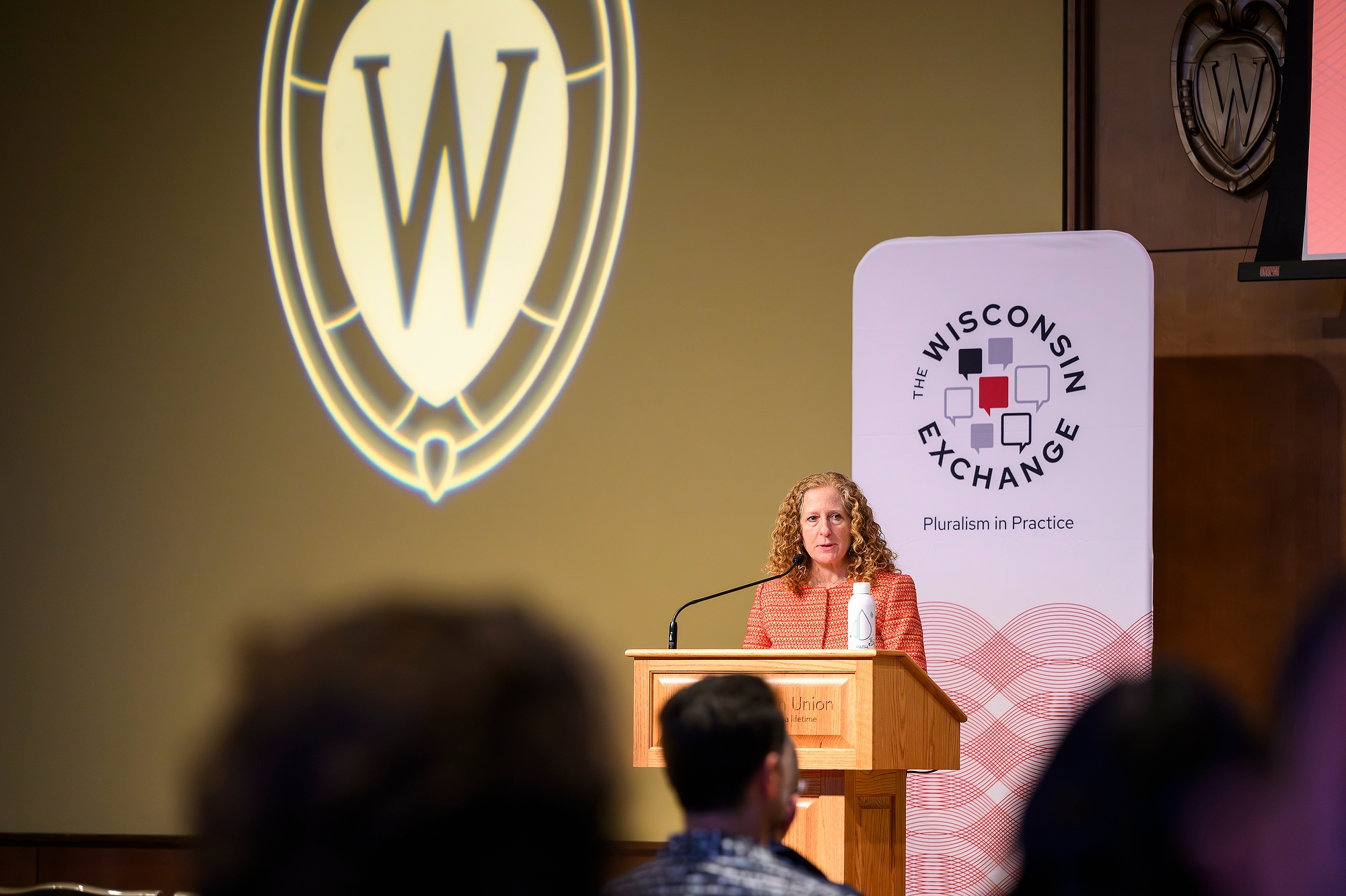 Chancellor Jennifer Mnookin speaks at a podium, with a banner behind her that reads "The Wisconsin Exchange: Pluralism in Practice"