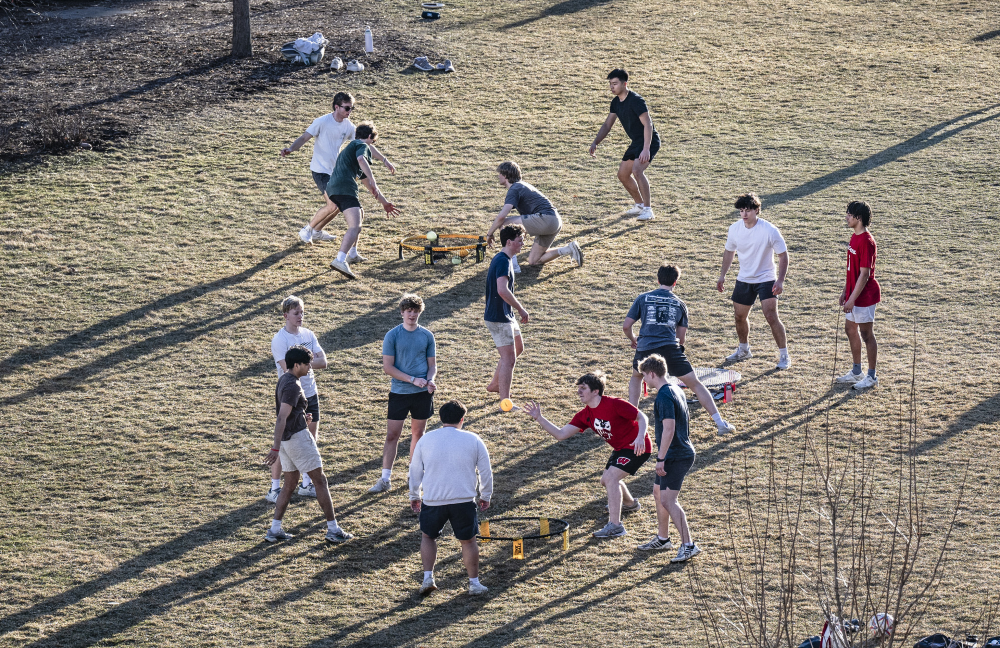 Fourteen people gather around three Spikeball nets playing the sport on a grass field. 