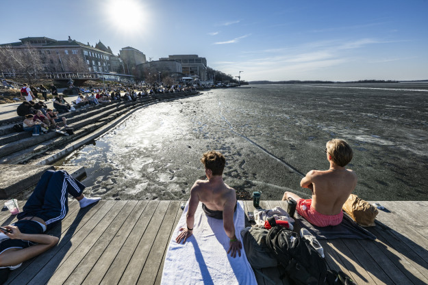 Two people in lounge on a pier on a sunny day with the lake partially iced over.