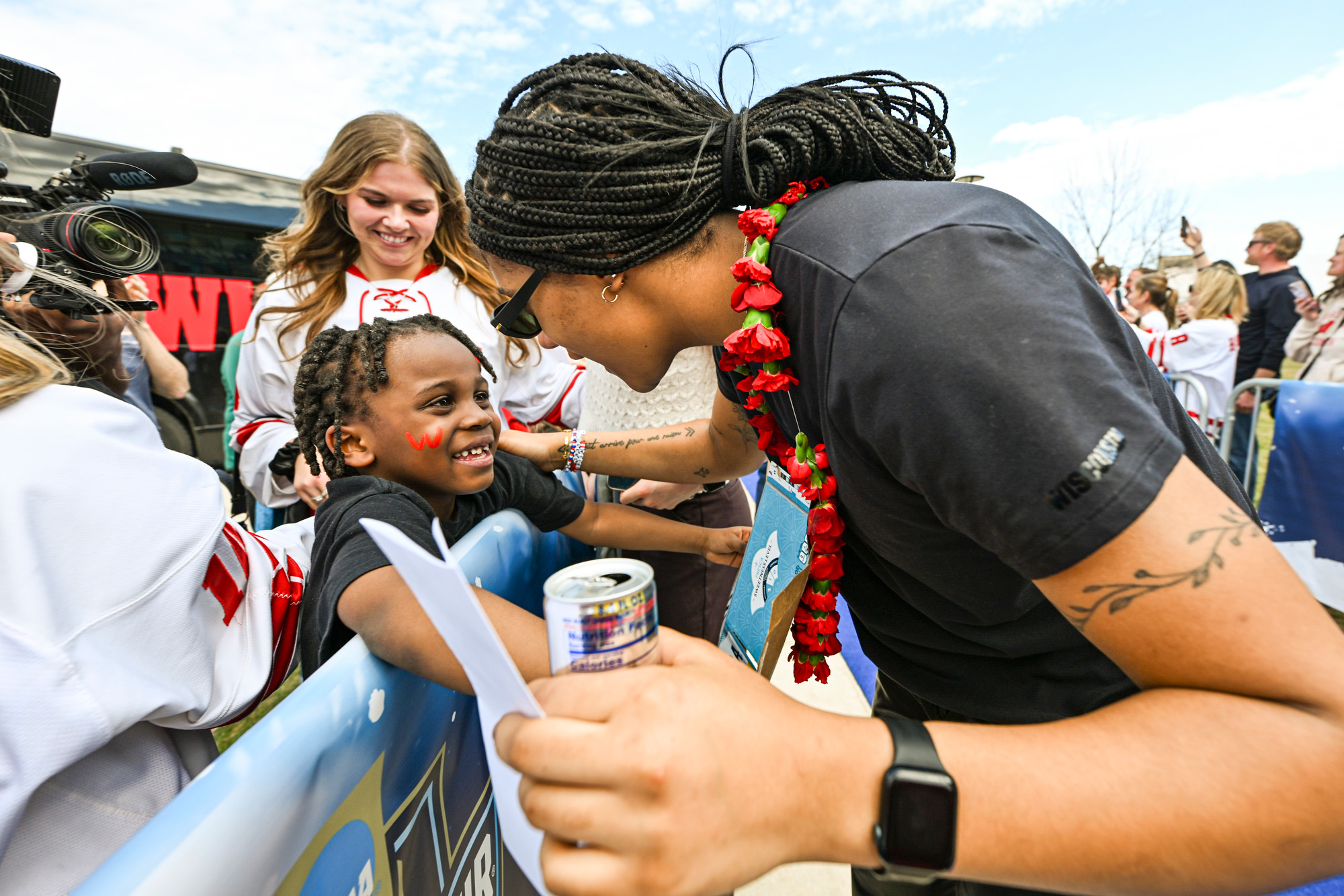Edwards holds up her hand for a high five with fans who stand behind a barrier that lines the blue carpet leading into the ice hockey arena.
