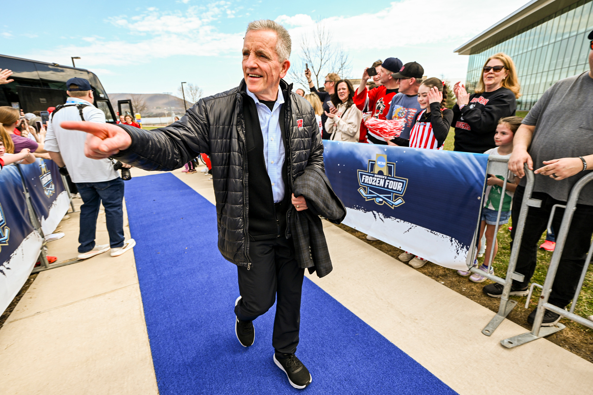 Johnson walks on a blue carpet that forms a path between the team bus and the ice hockey arena. He smiles and points to fans who stand behind a barrier that lines the blue carpet.