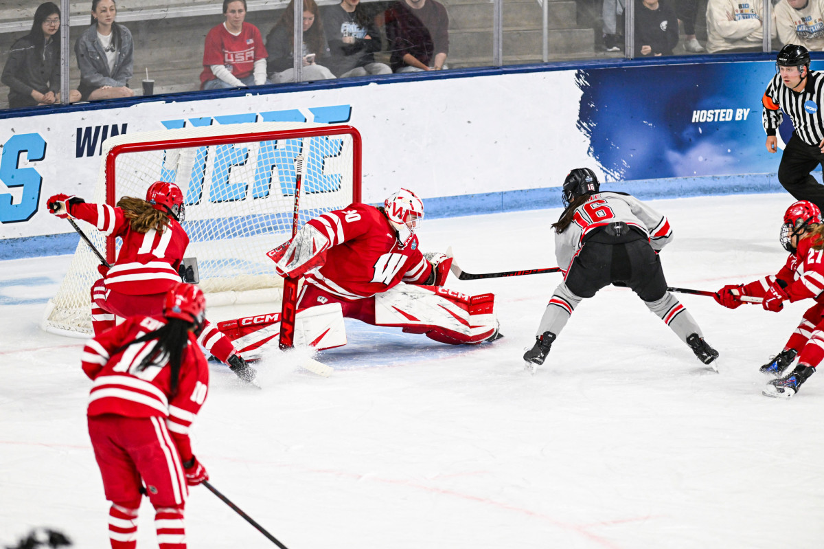 The goaltender for the Badger women’s hockey team does the splits with her legs to keep the puck from going by her and into the goal.