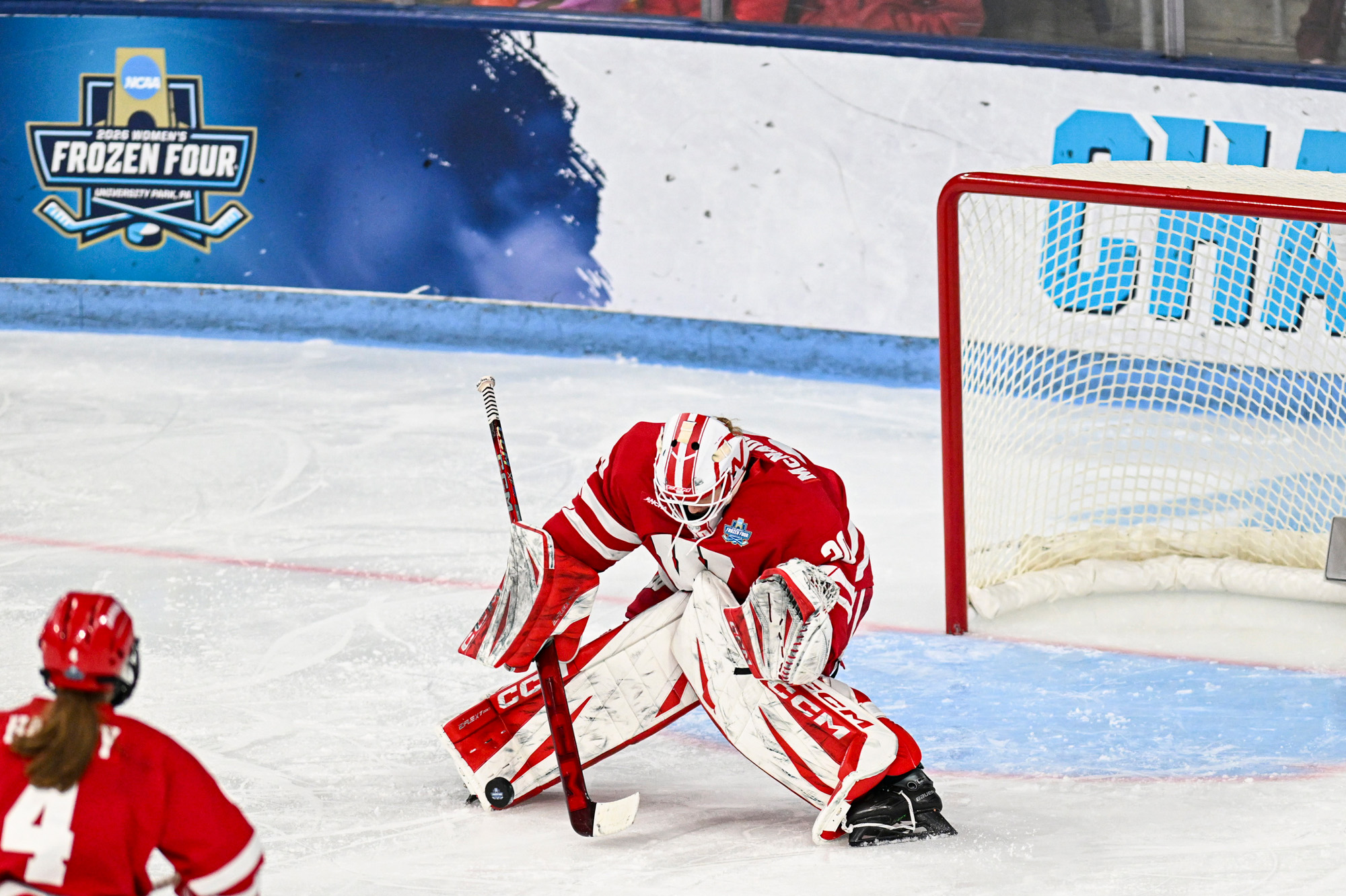 The goaltender for the Badger women’s hockey team blocks a puck with her leg pads to keep the puck from going by her and into the goal.