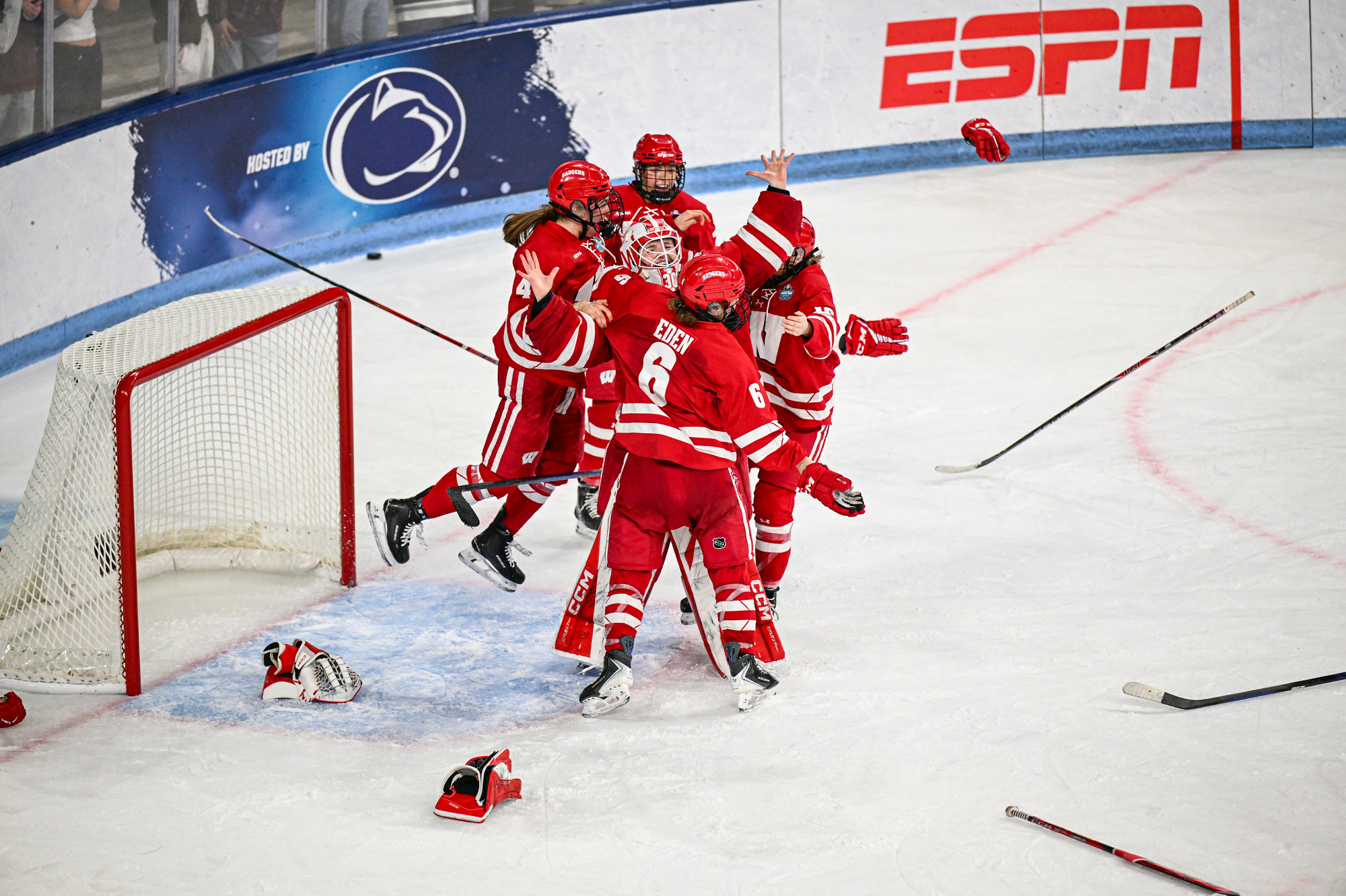 Five members of the Badger women’s hockey team jump up and down in front of a goal as they celebrate their win.