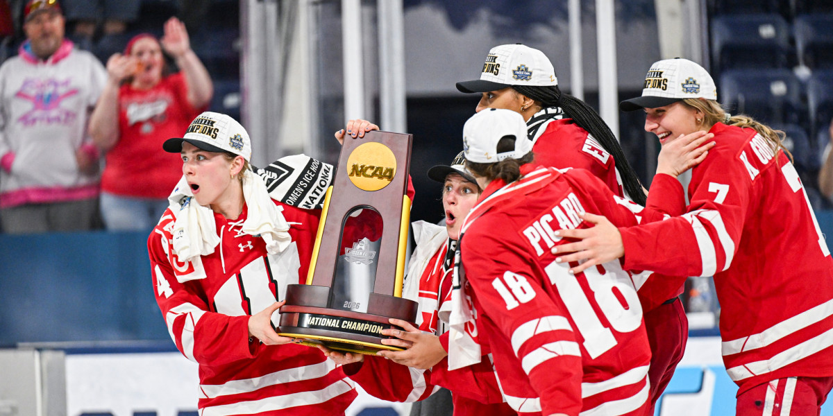 Five members of the Badger women’s hockey team hold up the NCAA championship trophy while their faces sport shocked expressions
