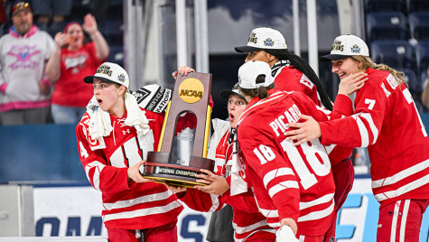 Five members of the Badger women’s hockey team hold up the NCAA championship trophy while their faces sport shocked expressions