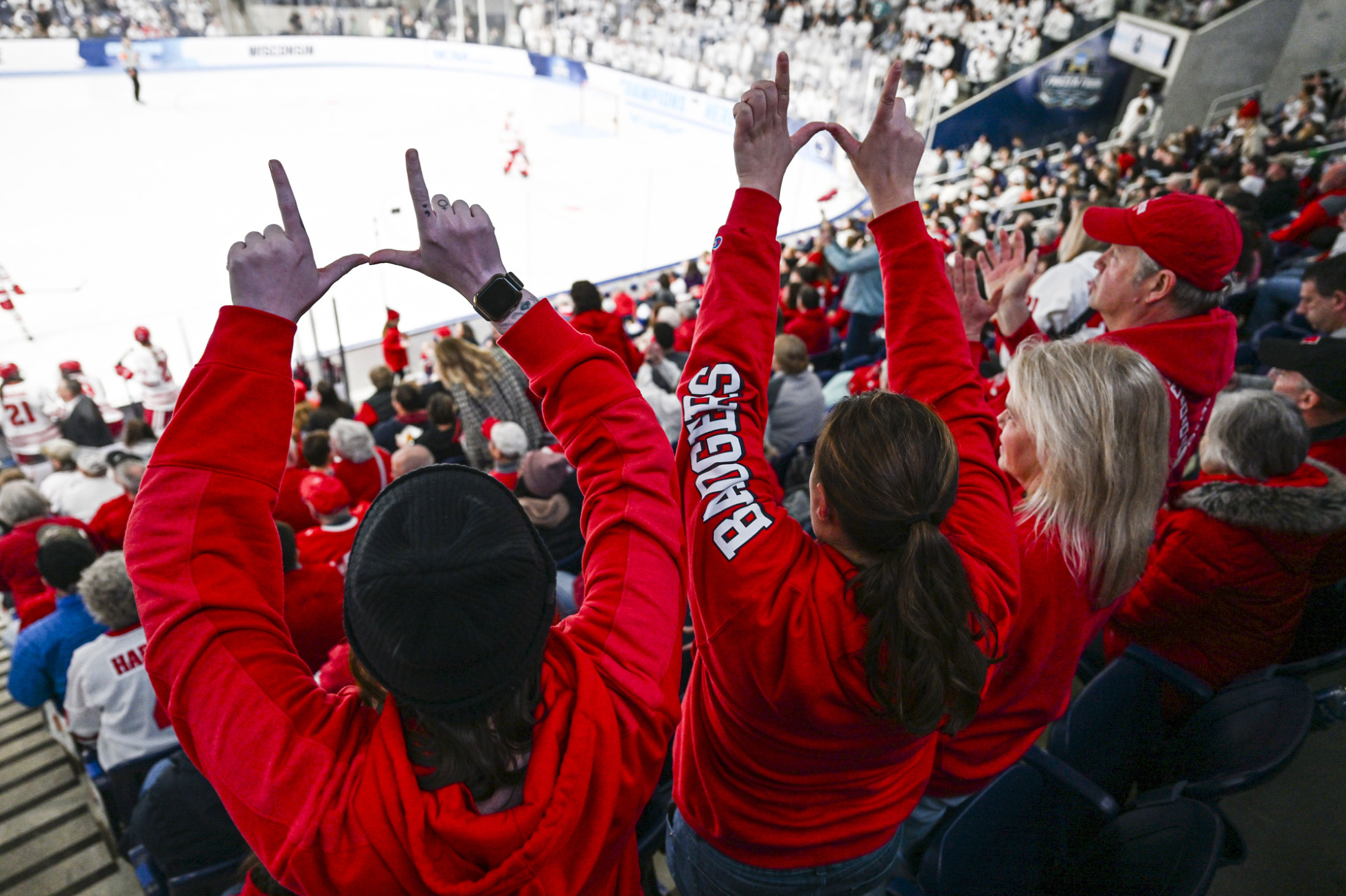 From behind, Badger fans hold up W signs with their hands in response to the Badgers scoring a goal.