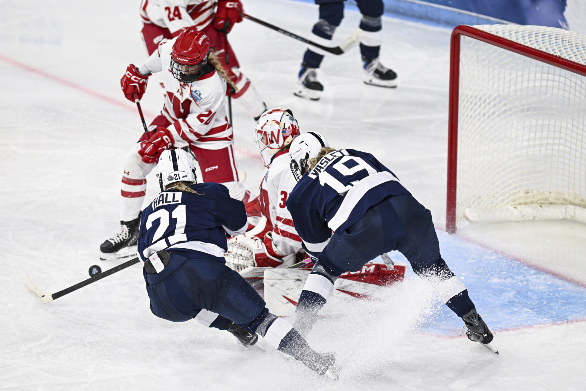 Two Nittany Lion hockey players surround Badger women’s hockey goalie as they attempt to score a goal.