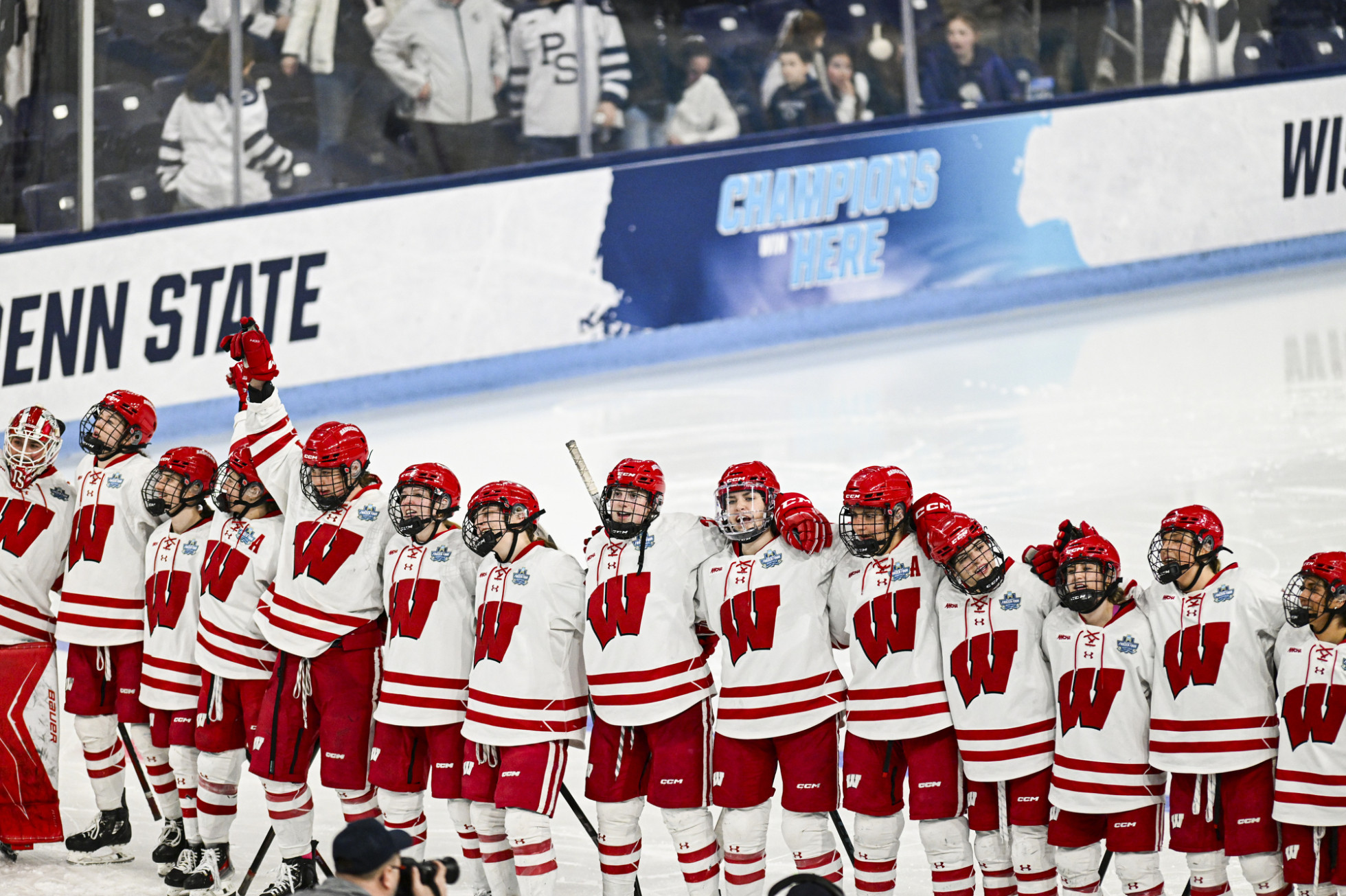 The Badger women’s hockey team stands linked arm-in-arm in a line on the ice as they sing the song Varsity.