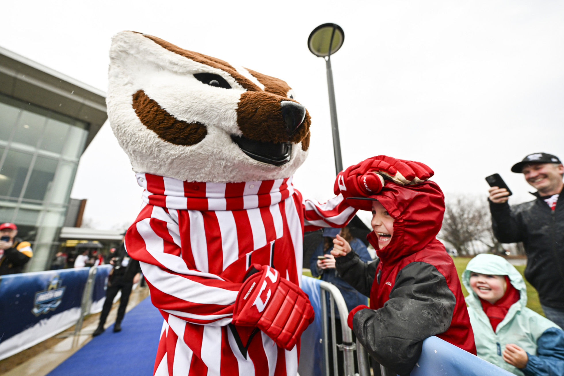 Mascot Bucky Badger pats a young hockey fan on the head while waiting for the Badger women’s hockey team to arrive to an ice hockey arena.