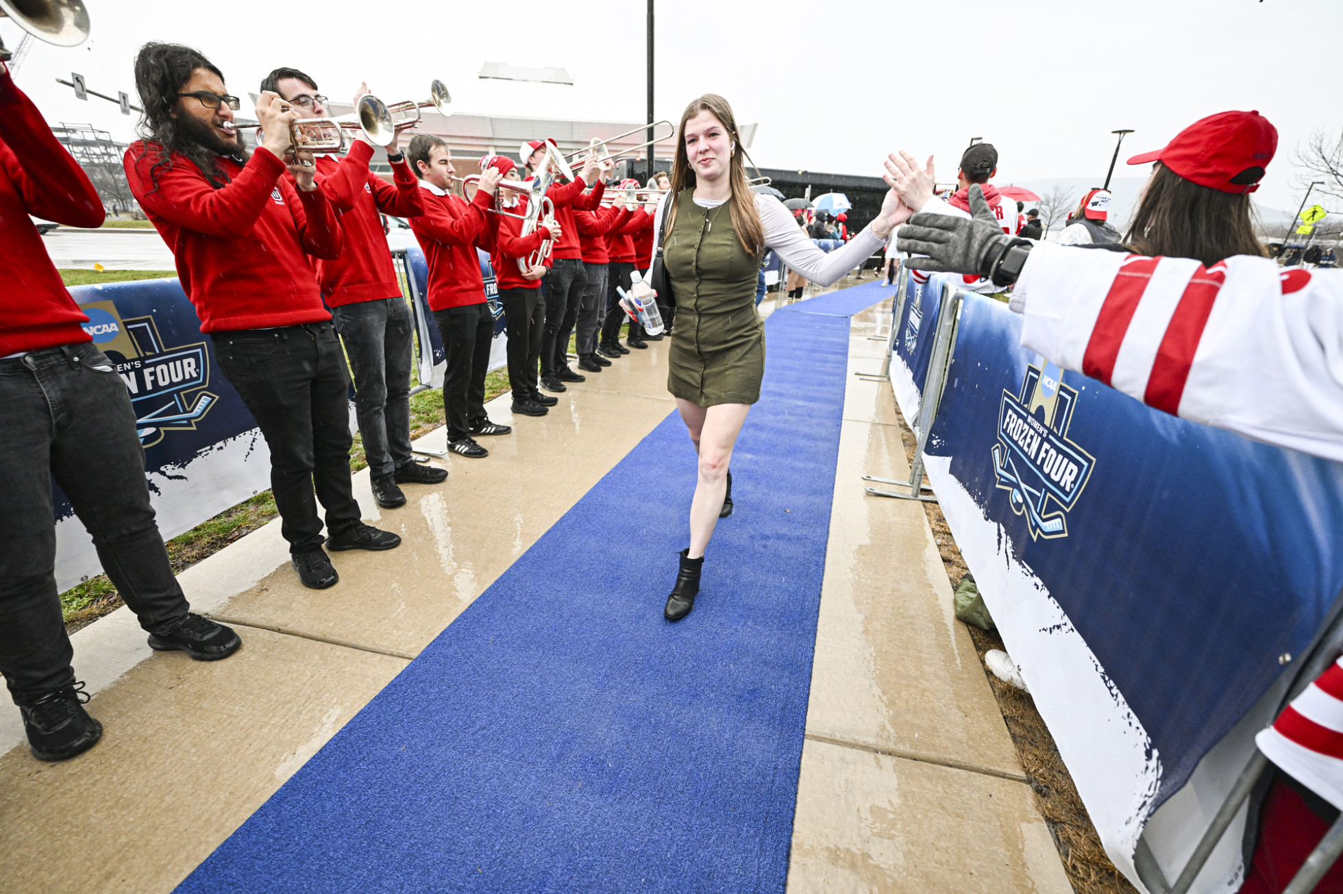Hockey fans and the UW Marching Band form a line from the bus to the ice hockey arena while cheering and giving high fives to a Badger women’s hockey player, who walks into the arena.