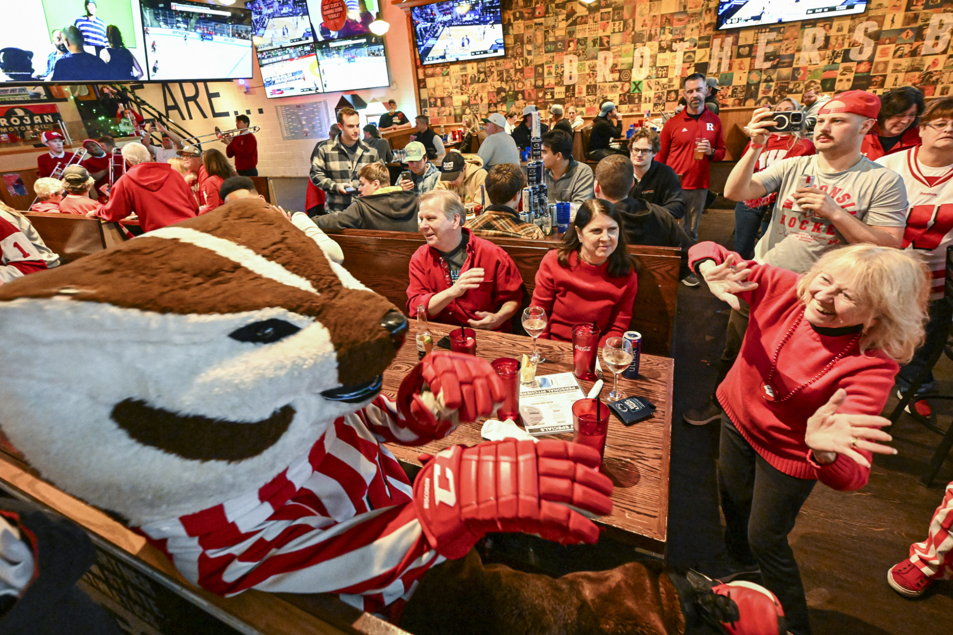 Mascot Bucky Badger sits in a restaurant booth and leads a family in a cheer for the Badgers. 