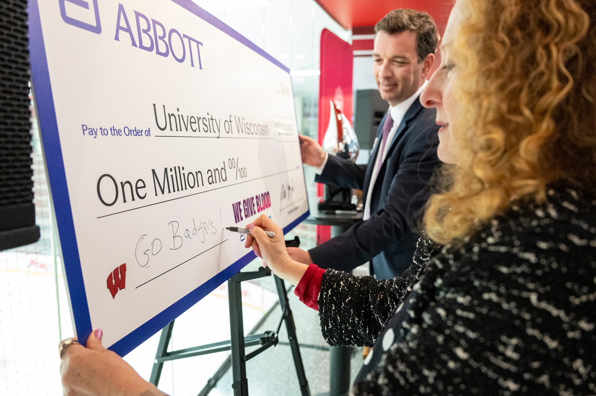Chancellor Mnookin signs an oversized ceremonial check that reads ‘University of Wisconsin – One Million and 00/100,’ while another person holds the check steady.