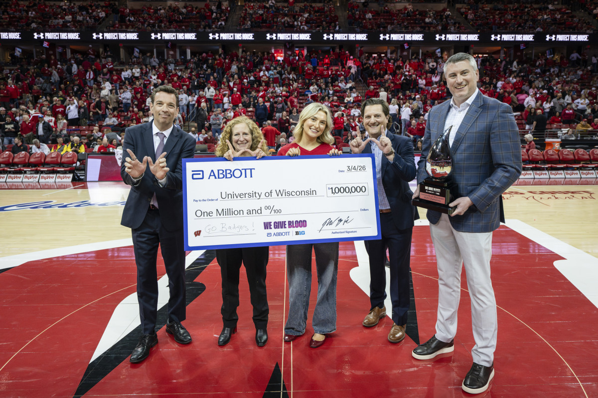 Five people stand on a basketball court during a game presentation, holding an oversized ceremonial check from Abbott to the University of Wisconsin for one million dollars.