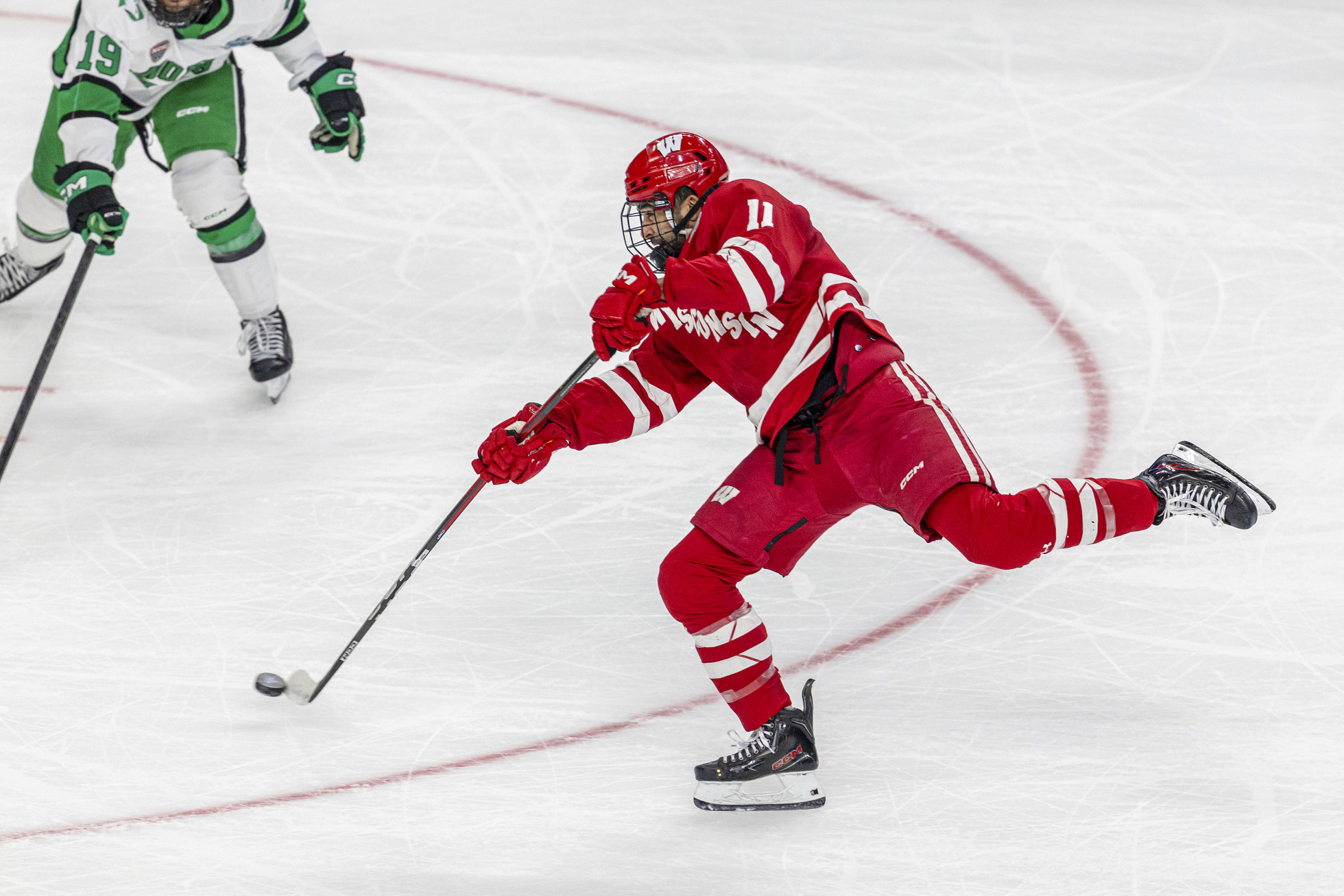 Wisconsin player 11 has the puck and leans foward on as he skates toward a North Dakota player.