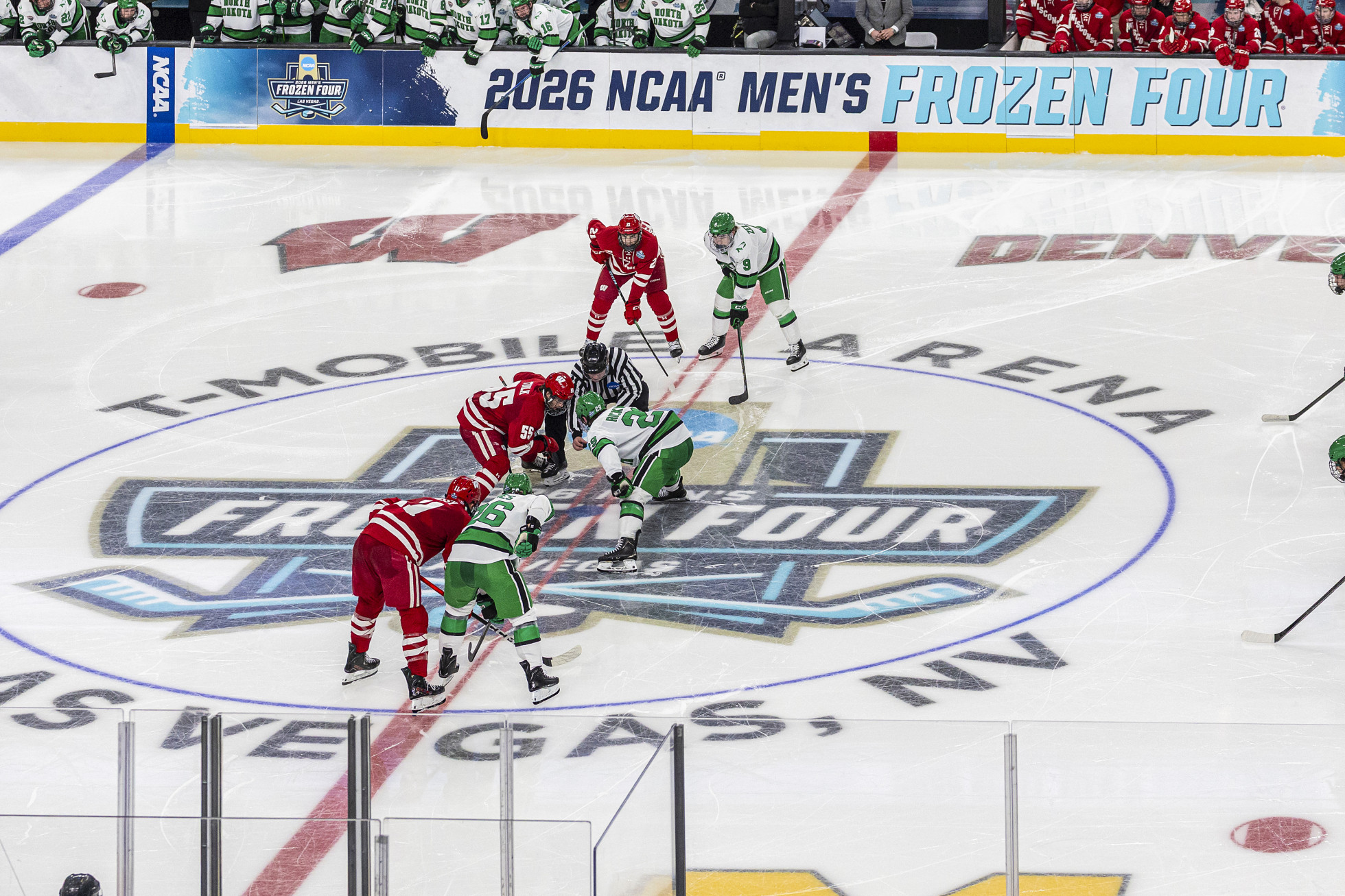 Three Wisconsin players face off for a puck drop against three North Dakota players at center ice.