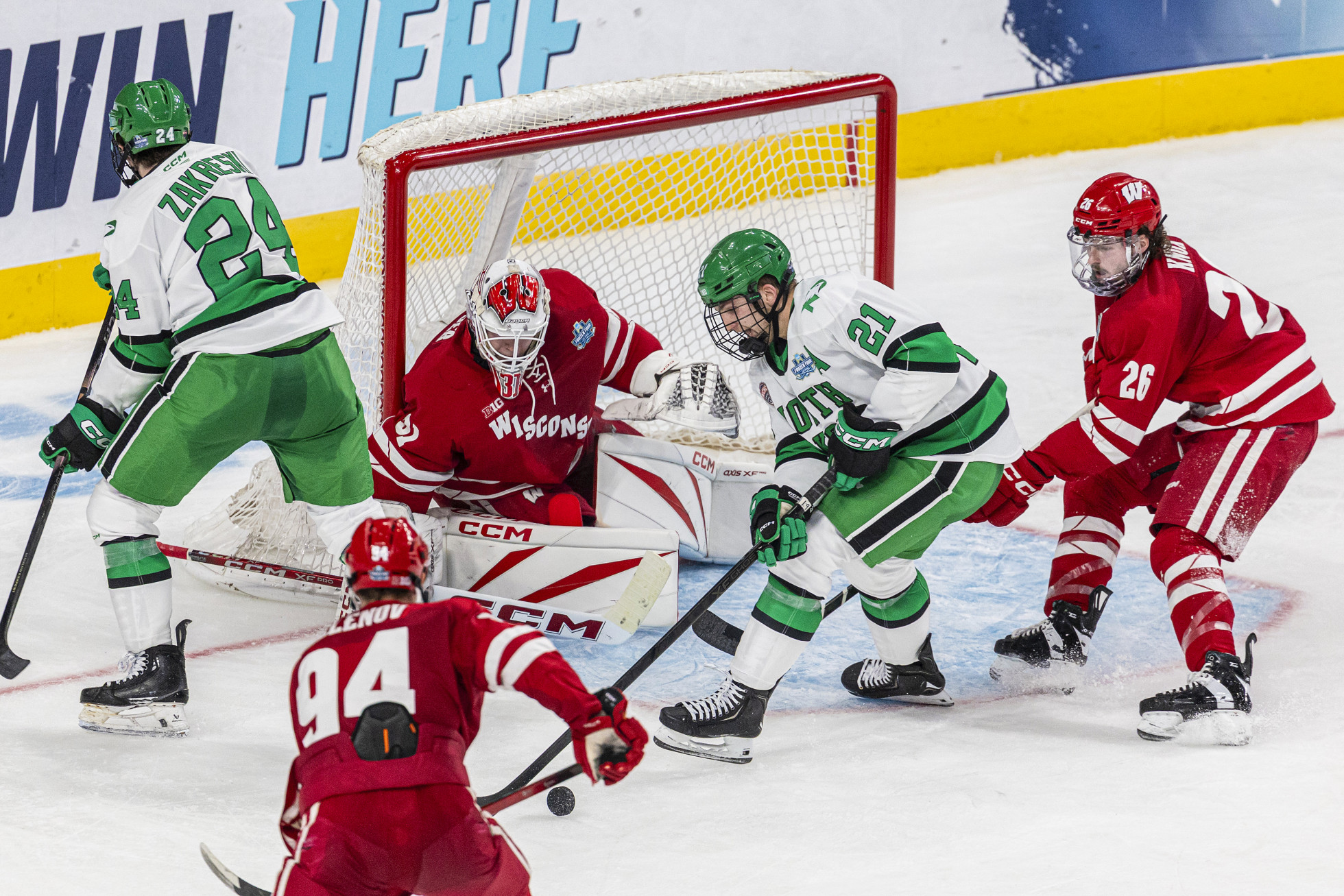 Two Wisconsin players and the Wisconsin goalie defend the net against two North Dakota players.