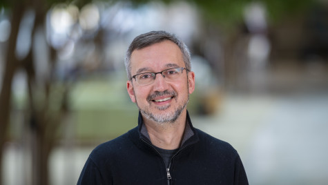 A portrait photo of a smiling man with graying hair and dark-framed glasses.