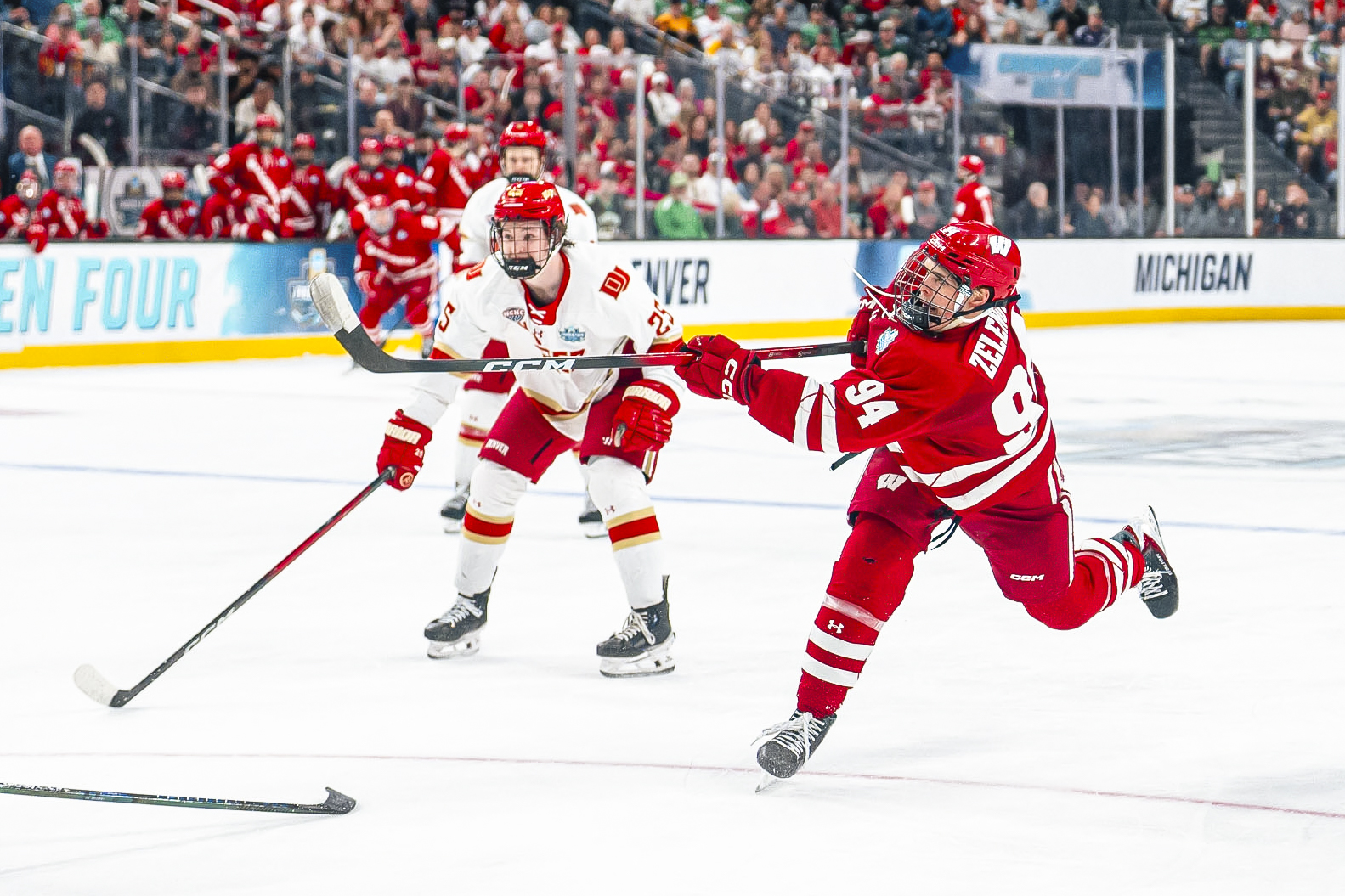 Wisconsin player 94 leans forward after taking a shot on Denver's goal. Two Denver players watch behind him.