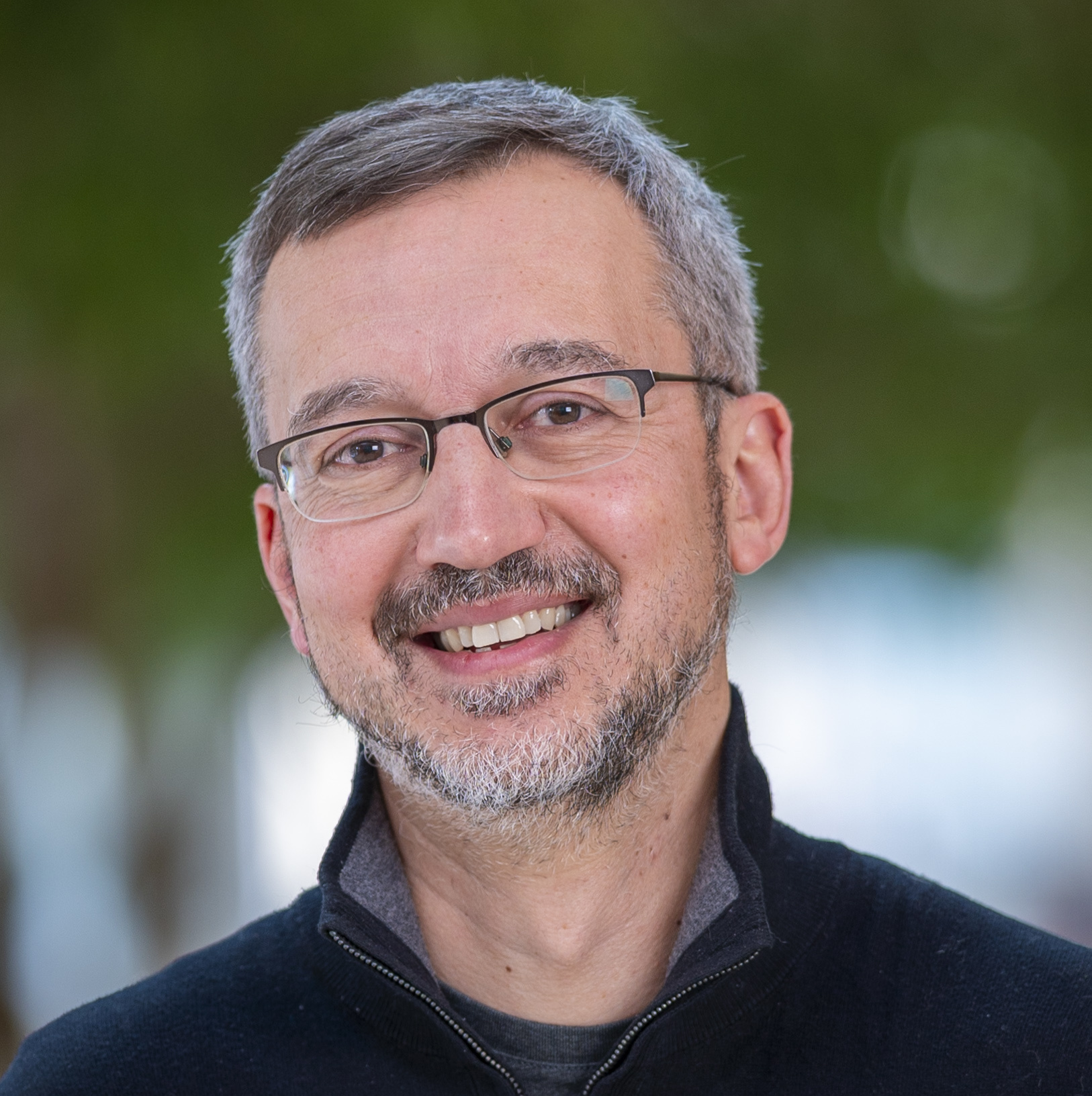 A portrait of a smiling man with graying hair and dark-framed glasses.