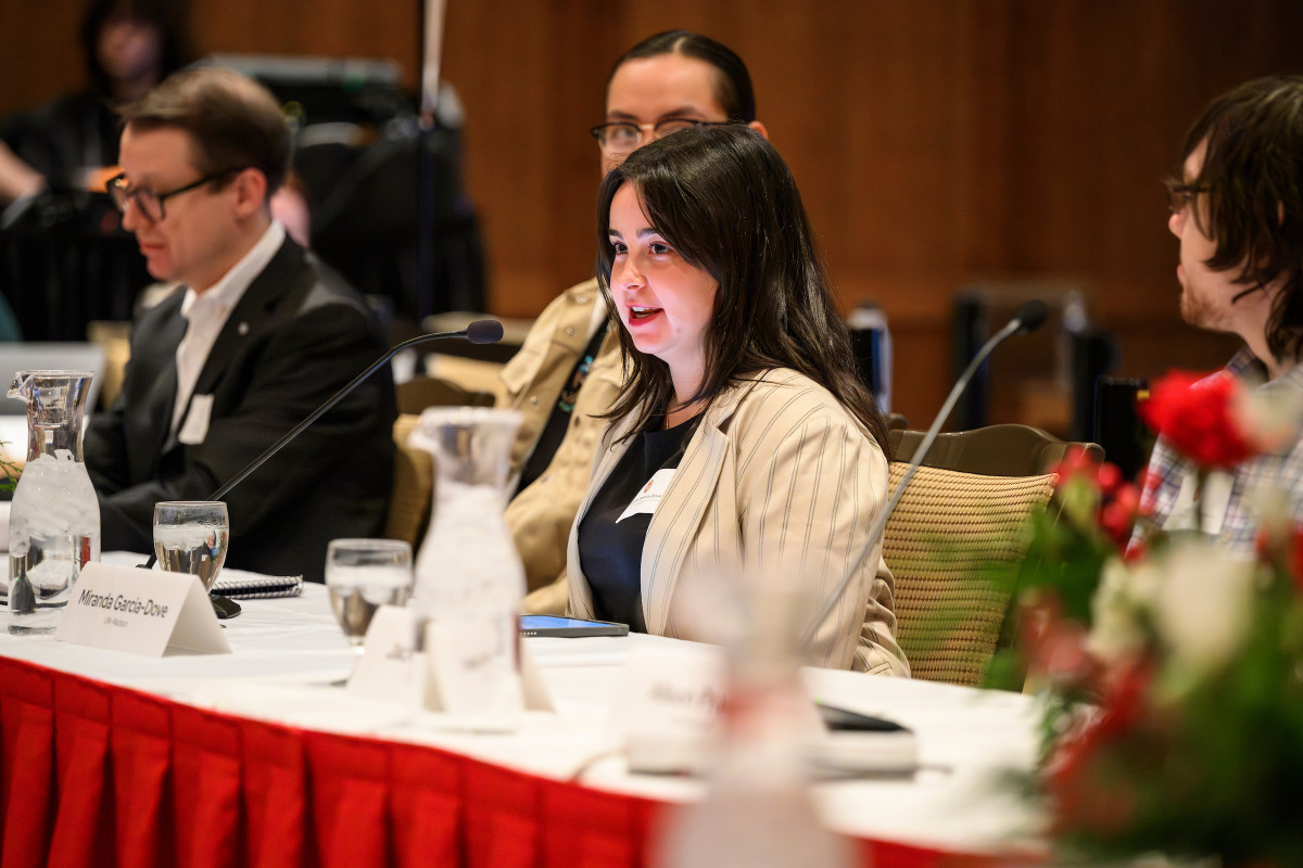 Garcia-Dove sits at a table as part of a speaking panel. She leans forward as she speaks into a table-top microphone.