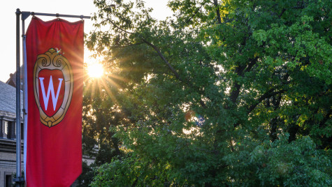 The sun emerges between a banner with the UW crest logo and a. tree line.