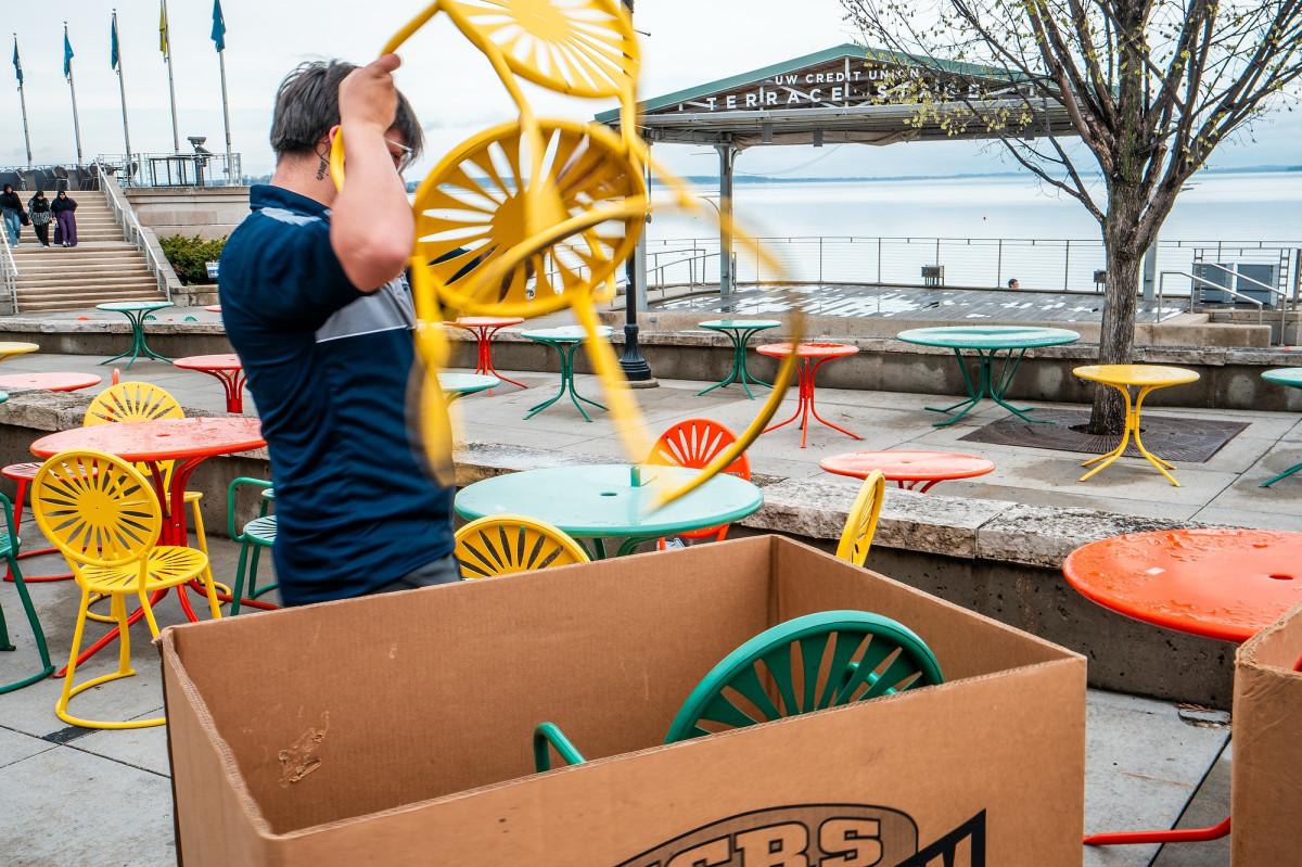 A worker carries a yellow sunburst chair while setting up the Memorial Union Terrace.