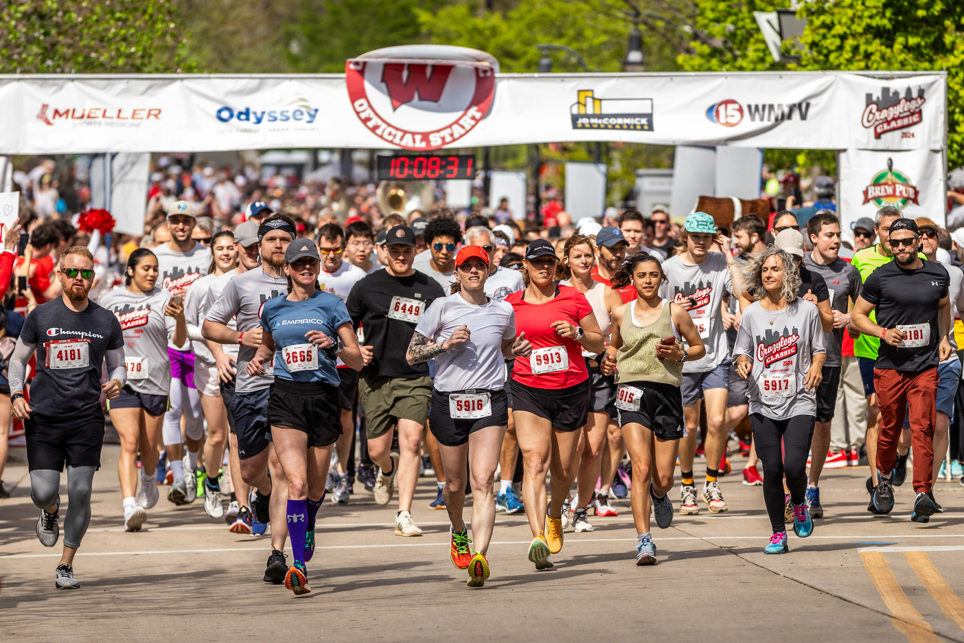 Dozens of racers take off with a starting line banner in the background.