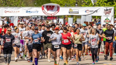 Dozens of racers take off with a starting line banner in the background.