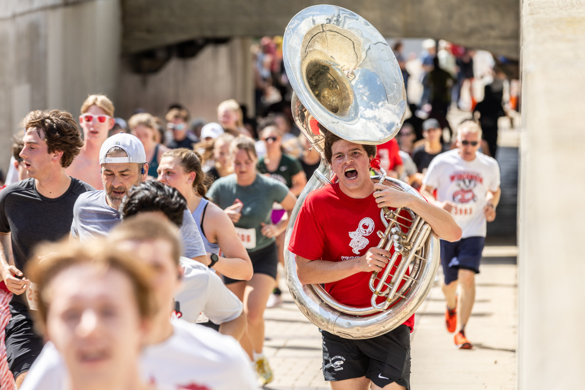 Racers run on a paved street, including someone holding a marching tuba. 