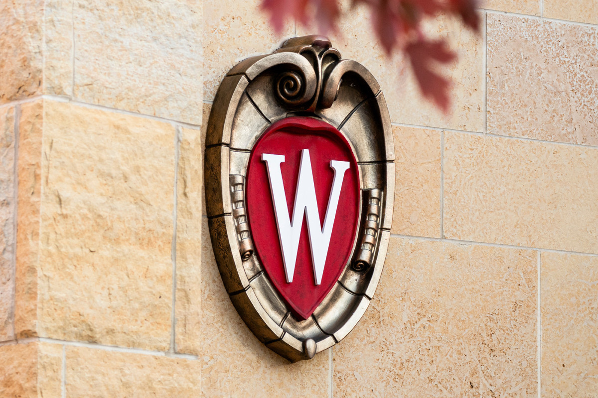 UW–Madison crest logo on the side of a building with red leaves peeking into the top of the photo.