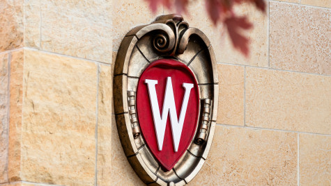UW–Madison crest logo on the side of a building with red leaves peeking into the top of the photo.