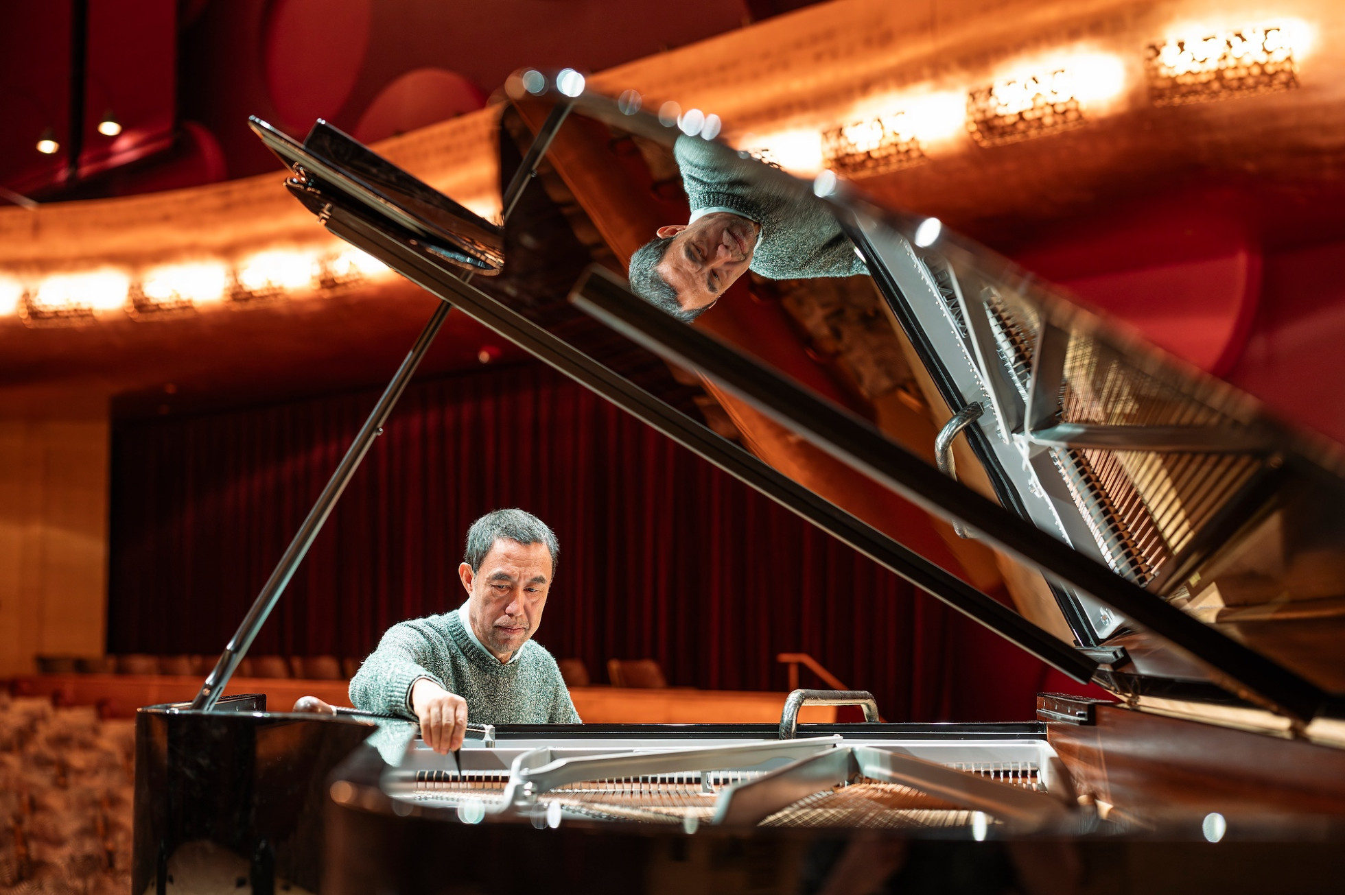 A person sitting at a grand piano making adjustments to the instrument
