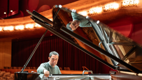 A person sitting at a grand piano making adjustments to the instrument