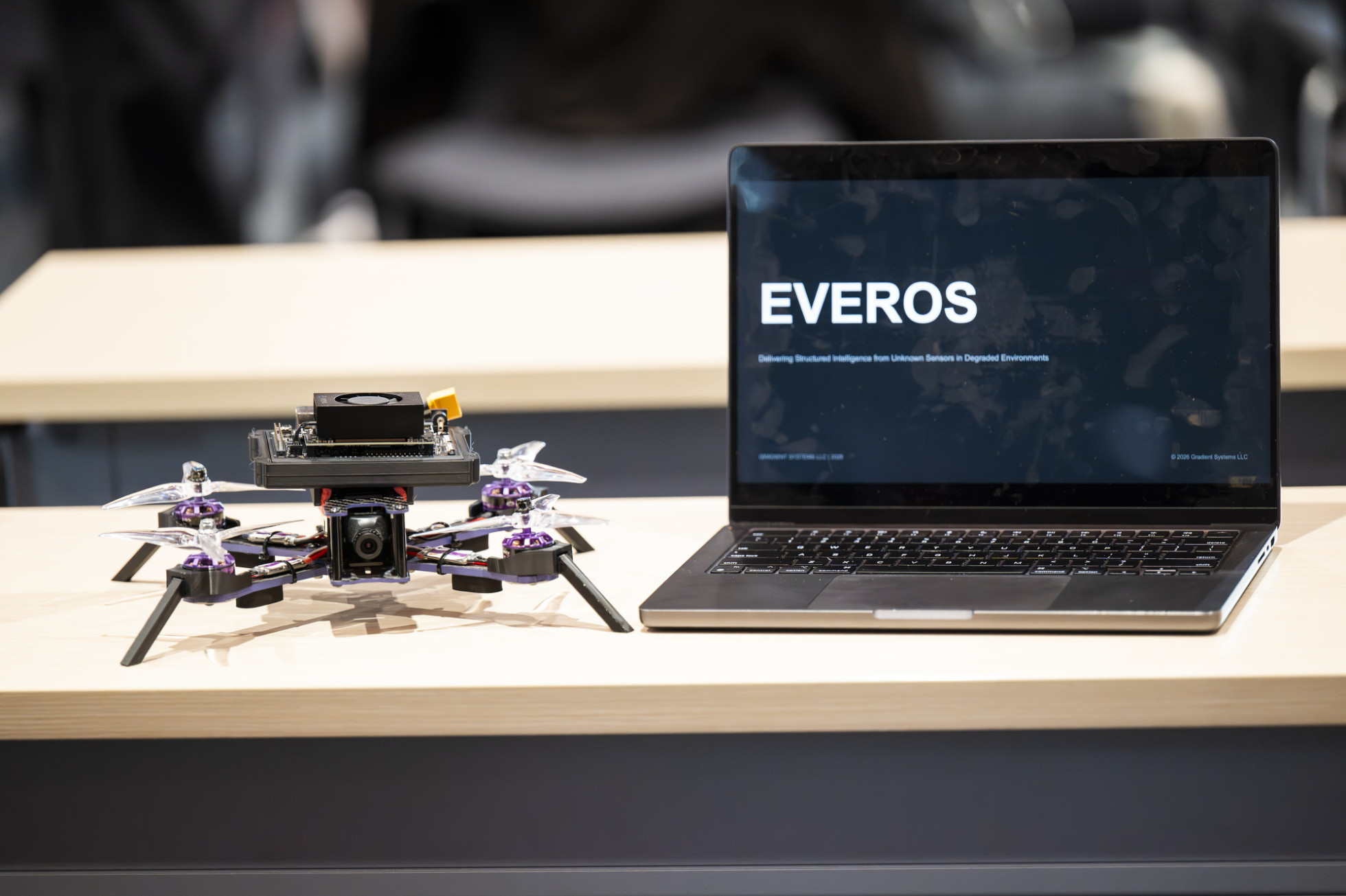 A small drone sits on a table next to a laptop.