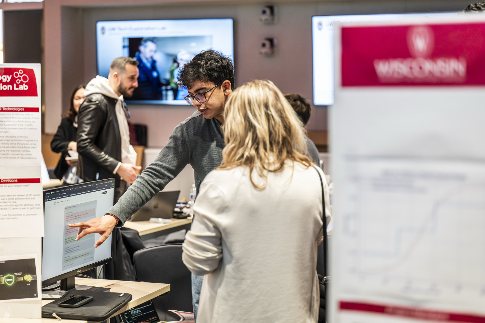 A student points to a computer screen as he explains something to a visitor.