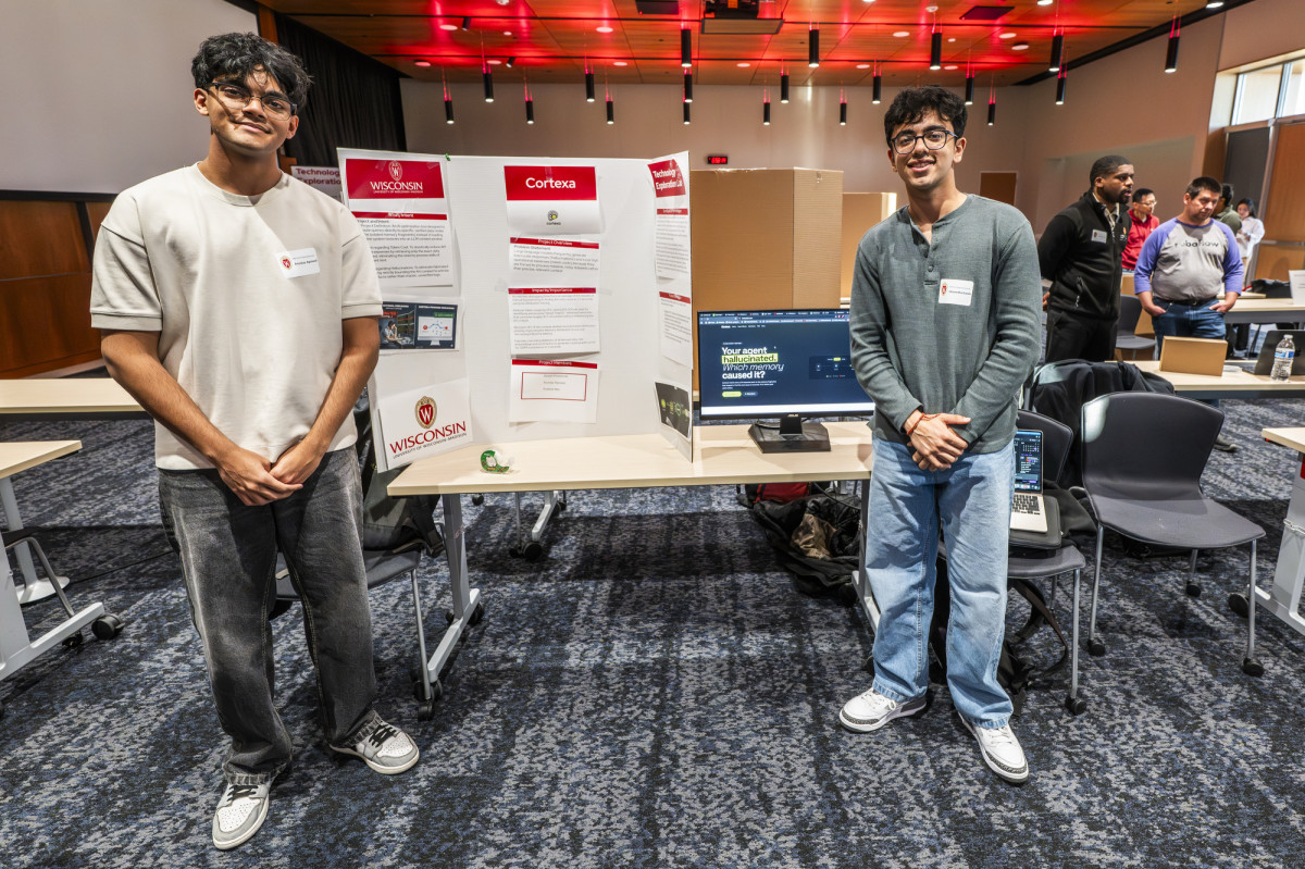 Two students smile as they stand on either side of their research poster.