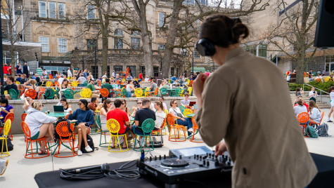 People sitting at tables on the Memorial Union Terrace, from the point of view behind a DJ on stage.
