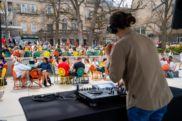 People sitting at tables on the Memorial Union Terrace, from the point of view behind a DJ on stage.