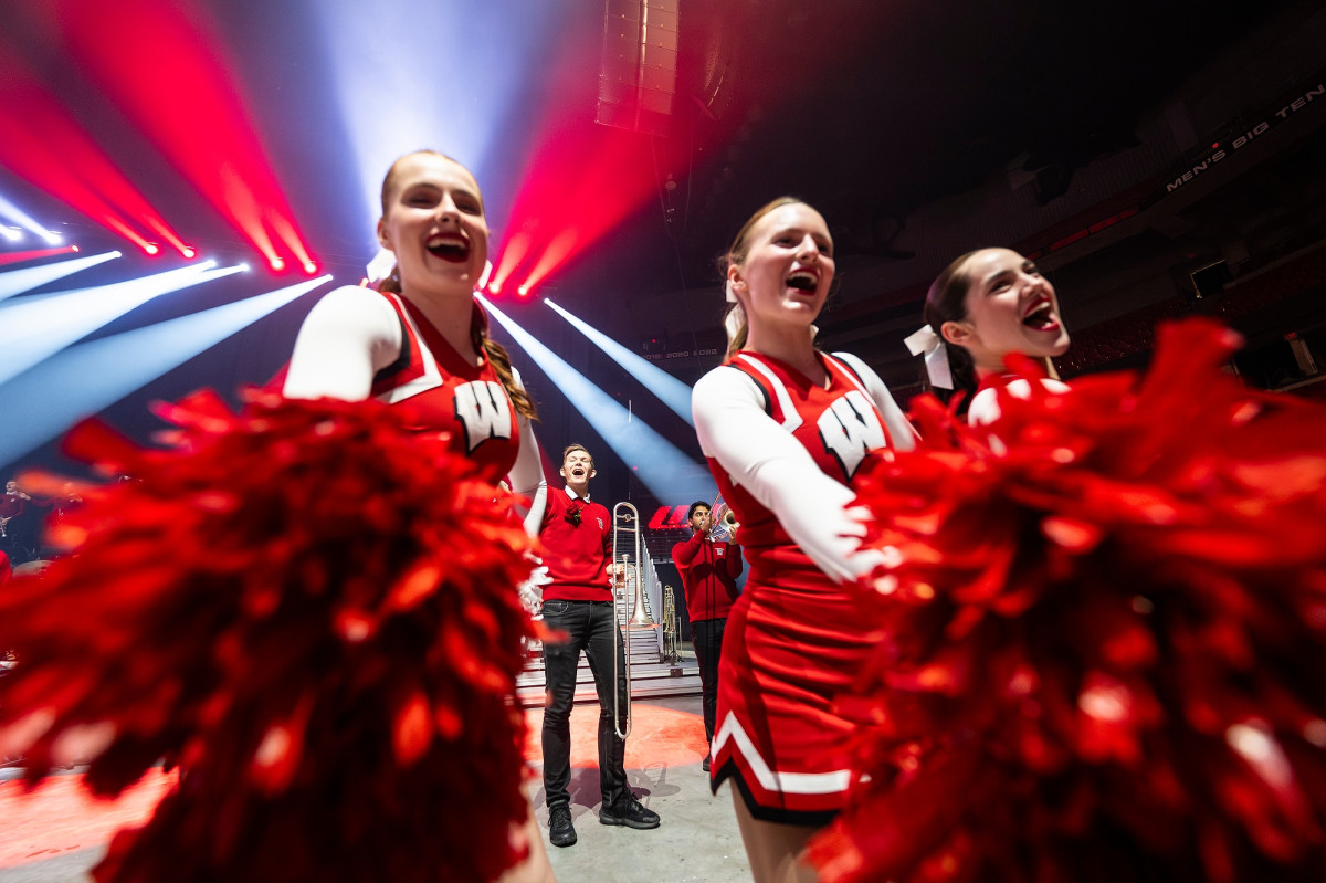 Three members of the UW Spirit Squad hold their red pom poms to the camera.