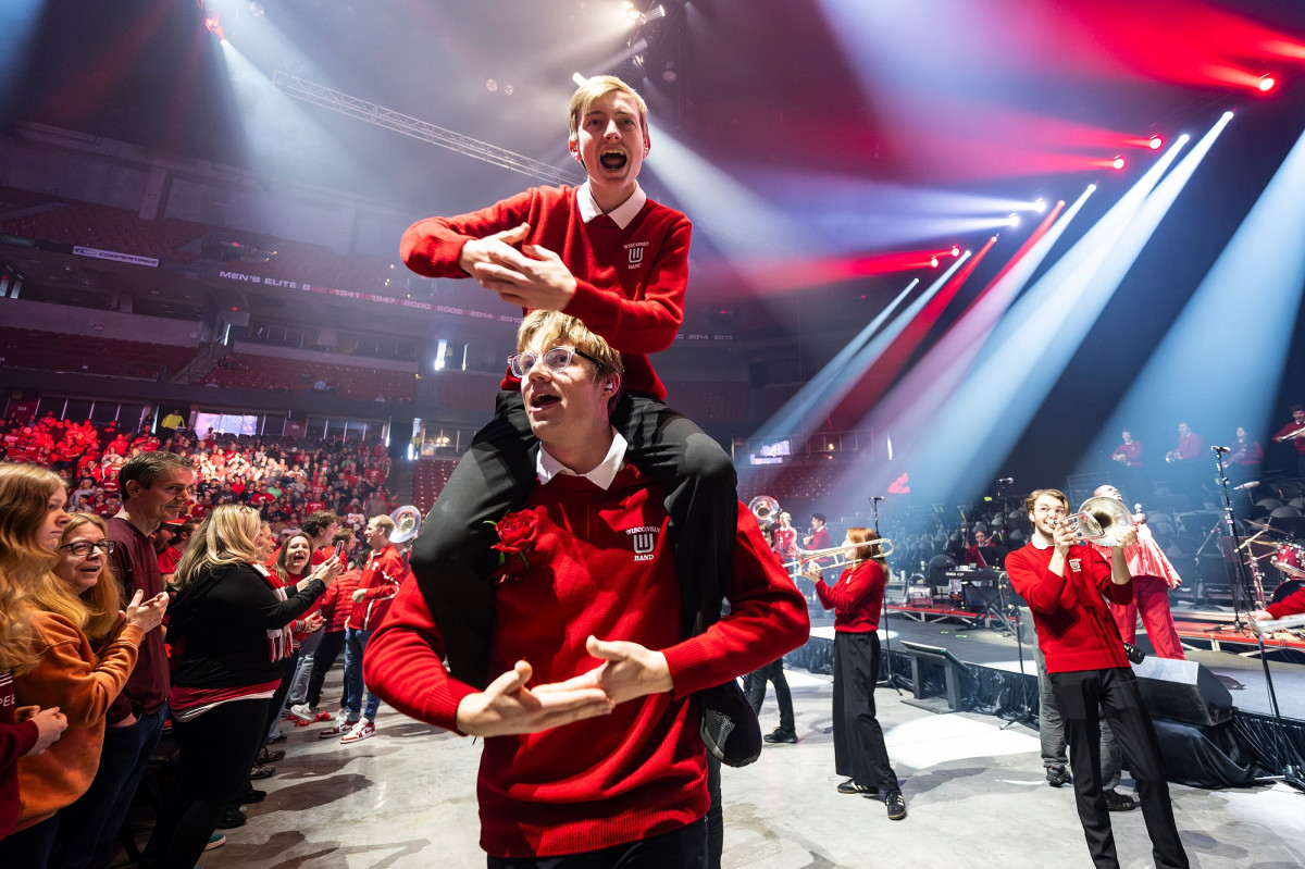 One member of the UW Marching Band holds a fellow member on his shoulders as they form their arms into a baby cradle.