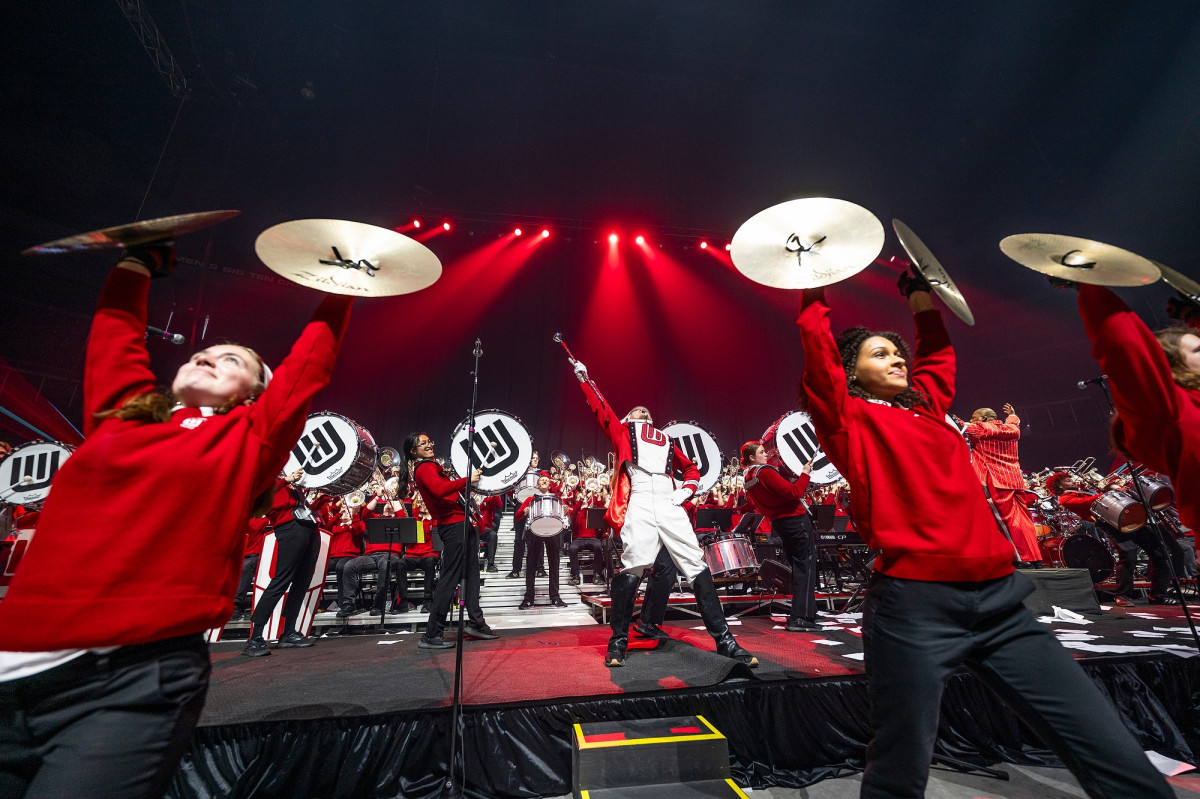 Member of the percussion section hold big bass drums and large symbols as they pose at the end of a song.