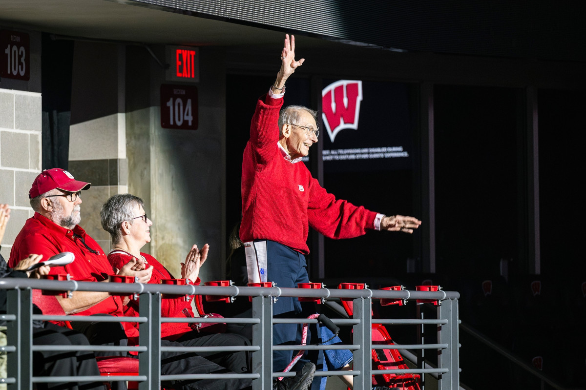 Leckrone wears a red UW Marching Band sweater and stands to wave at the crowd.