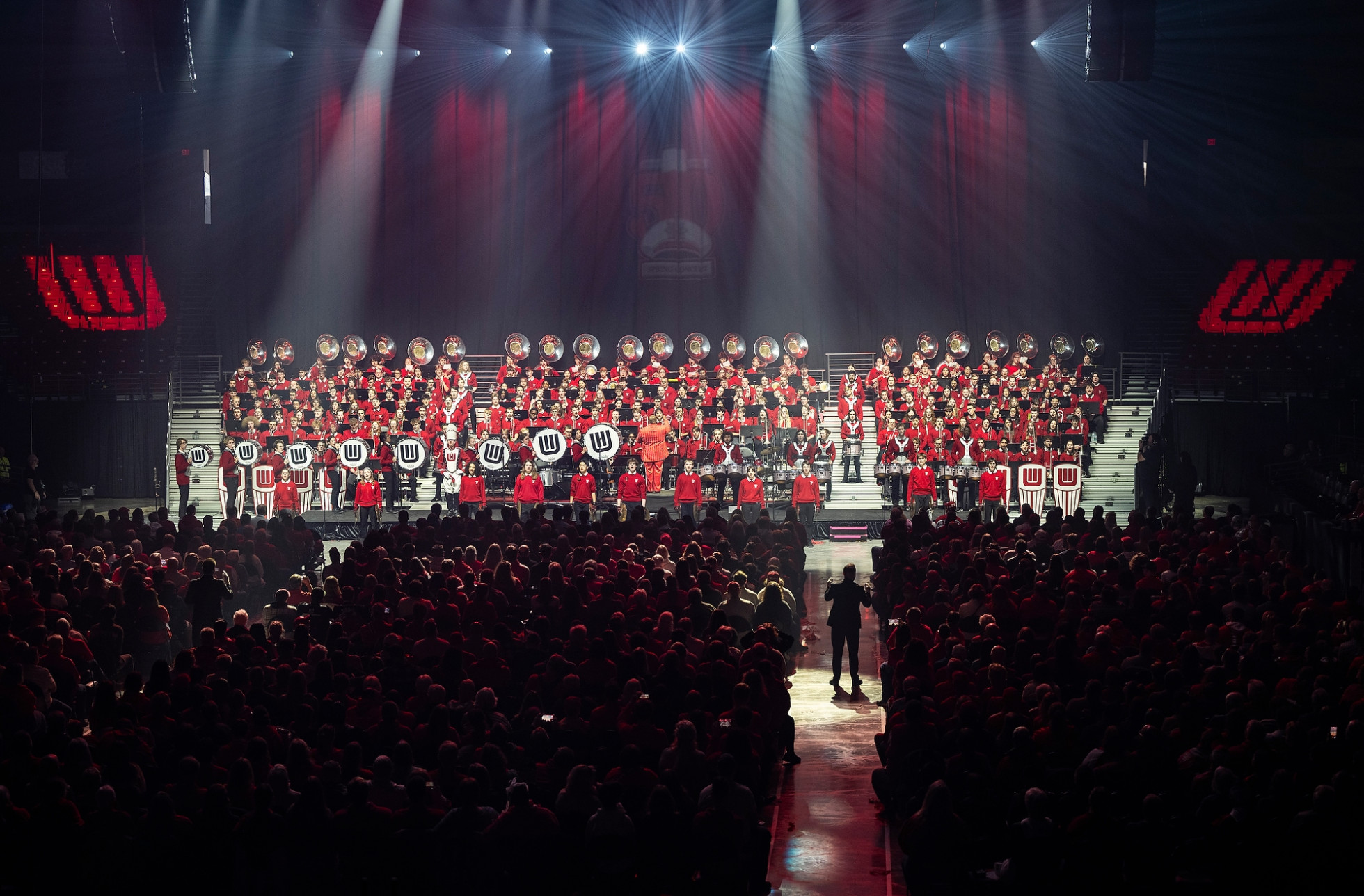 An overhead image shows a full Kohl Center seated to watch the UW Marching Band perform on stage.